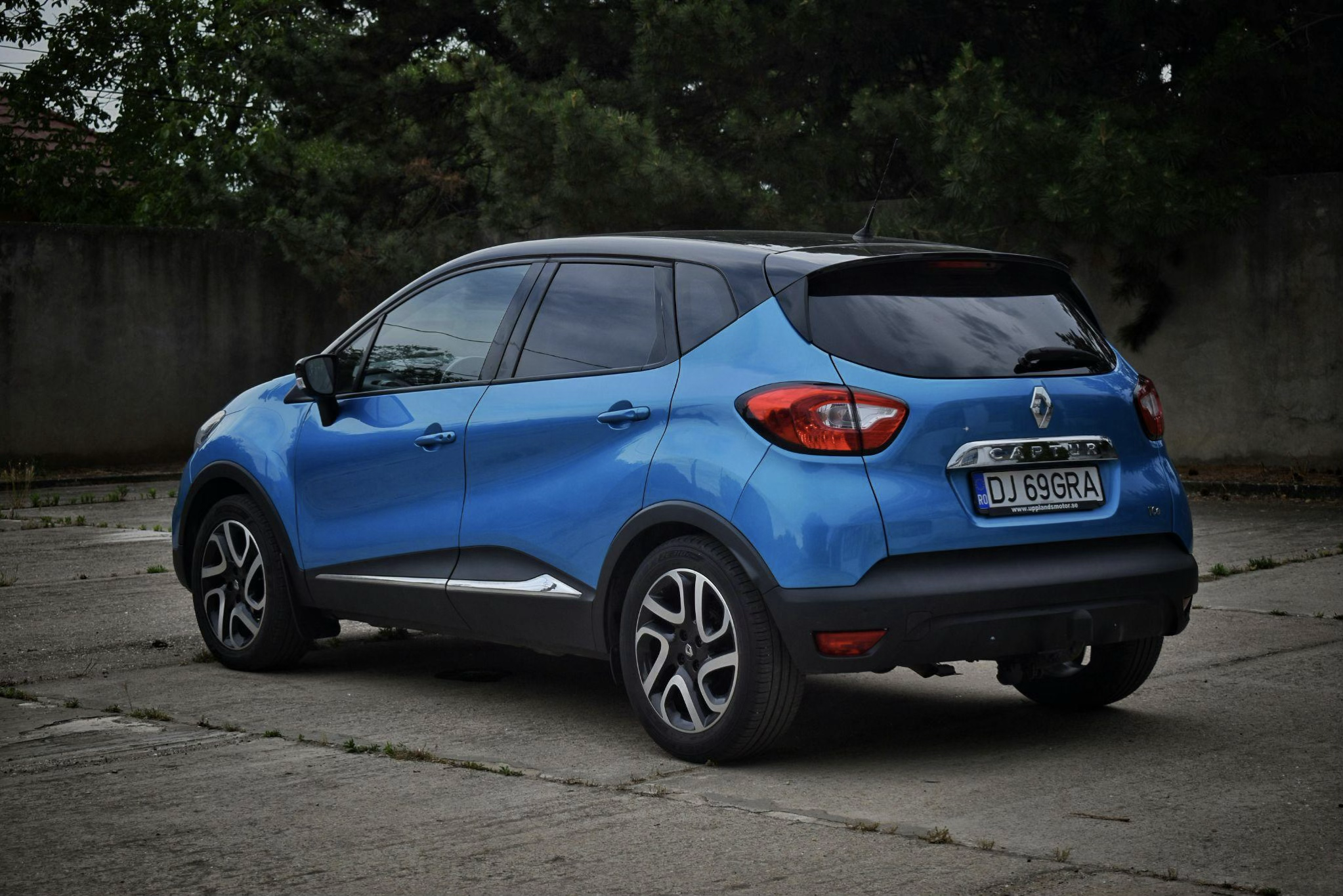 Vue arrière trois-quarts d'un Renault Captur bleu métallisé avec toit noir, stationné sur un parking